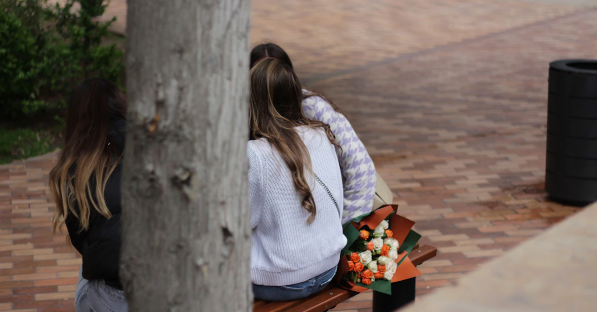 two women sitting on a bench with flowers