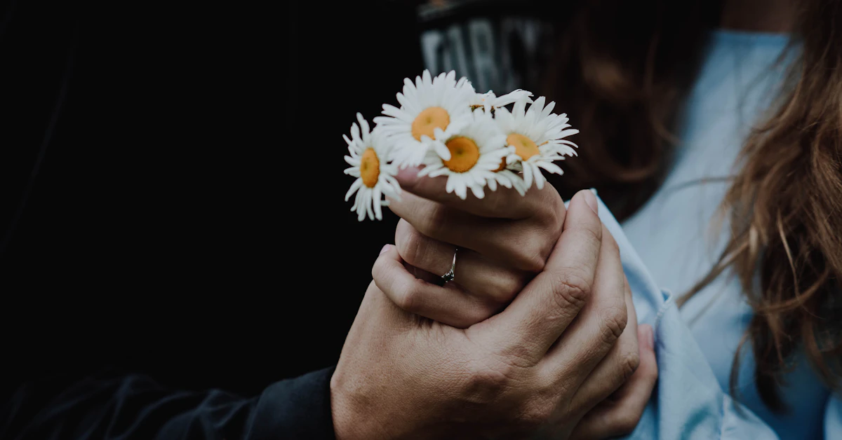 low-light photo of man holding the hand of woman holding white daisies