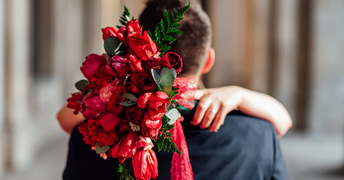 man hugging woman carrying red flower bouquet